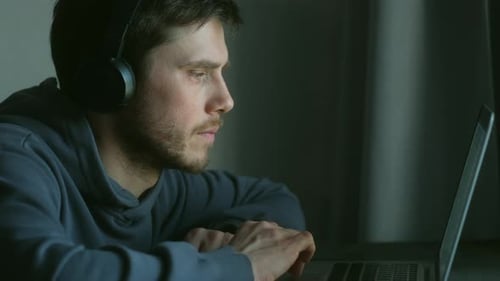 Pessoa está sentada em uma mesa com um laptop com fones de ouvido