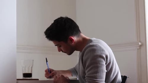Man Writing in Notebook, Drinking Coffee Indoors