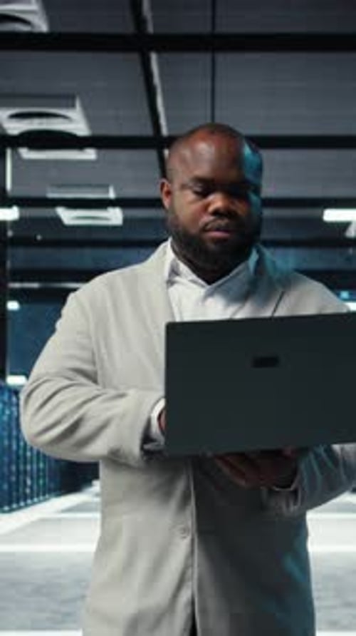 Vertical Video Engineer Walking in Server Room Backing Up Storage Arrays Using Software