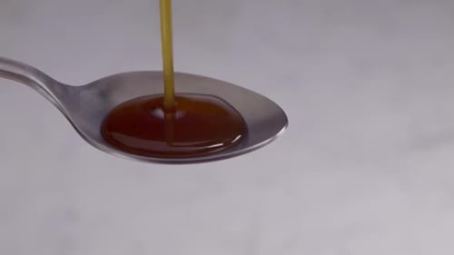 Thick Brown Syrup Honey or Medicine Pouring onto a Silver Spoon