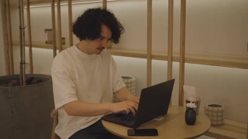 Seitenansicht eines Mannes, der tagsüber im Café sitzt und den Laptop für den Telearbeit als Freelancer benutzt