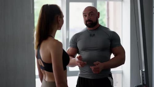 A Man Fitness Trainer and a Girl Client in the Gym Have Contented Conversation After Finishing a
