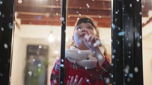 Adorable child look through the window and admiring first snow flakes.