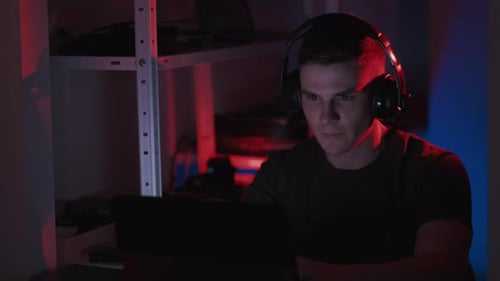Man Wearing Headphones Looks at Laptop at Night