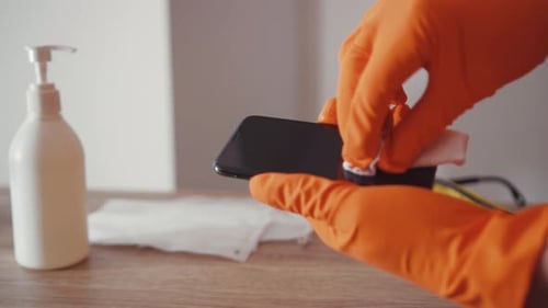Hands in Gloves Cleaning a Cell Phone Screen