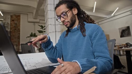 Biracial Architect Making Changes in Floor Plan Using Laptop in Office