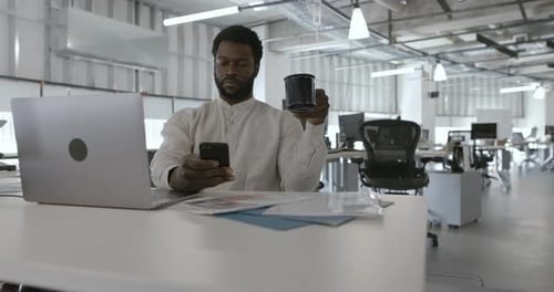 Businessman Drinking Coffee and Using Smart Phone at Office Desk Businessman