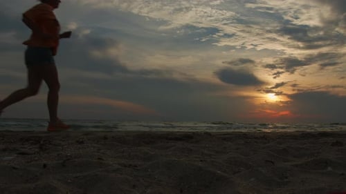 Woman jogging along beach at sunset. Evening run in nature for health.