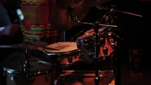 Drummer playing on a dark stage beats alternate sticks on drum, percussion, cymbals, snare drum