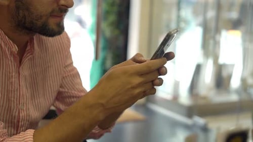 Young Man Texting on Smartphone Sitting in Cafe 30s