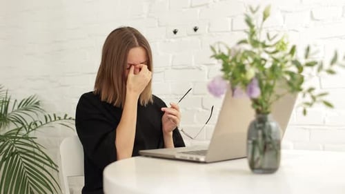 Tired young woman worker student take short pause in online work remove glasses, rubs eyes and massa