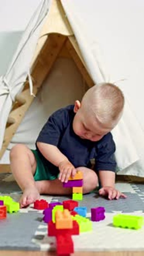 Un niño pequeño se sienta en su casa sobre una alfombra y construye una torre a partir de un set de construcción