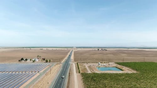 A rising shot of a rural road surrounded by solar panels on the left hand side and vineyards on the