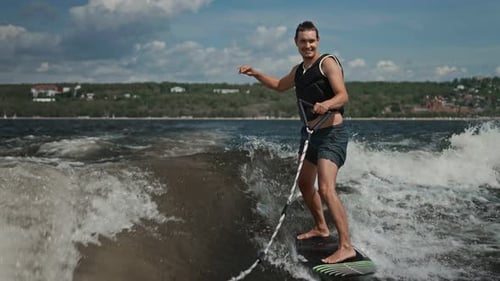 Ein junger, attraktiver Mann lernt Wakesurfen hinter einem Boot. Unterhaltsame Wasseraktivität im heißen Sommer