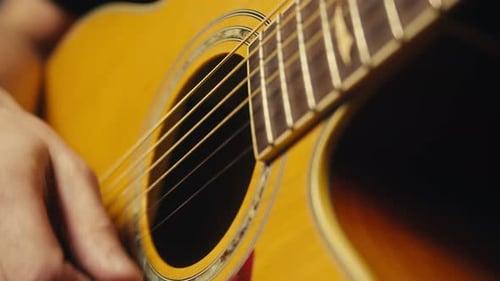Young Musician Man Sitting and Playing Acoustic Guitar Among Music Equipment in Studio Closeup