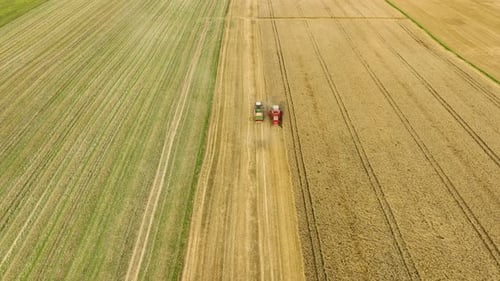 Aerial view of a combine harvester and tractor working in a wheat field, showcasing the coordinated