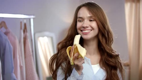 Smiling woman eating a banana in her room