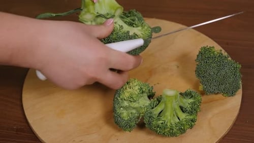Closeup of a Woman Cutting Broccoli on a Wooden Chopping Board in the Kitchen