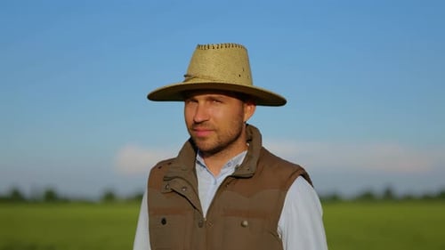 Smiling Farmer in Hat Standing in Green Field