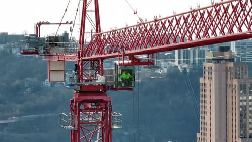 Opérateur de grue à tour contrôlant une grande grue rouge construisant un gratte-ciel dans le centre-ville américain.