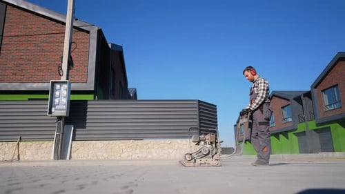 Worker Operating Plate Compactor on Paved Street