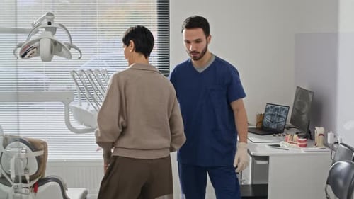 Young Dentist Inviting Patient to Treatment Chair in Modern Clinic