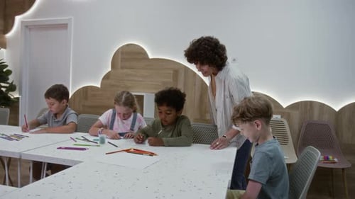 Teacher Helps Children Drawing at Classroom Tables