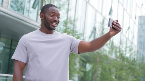 African American Man Holding Smartphone Having Video Chat on Urban Street in City Guy Blogger