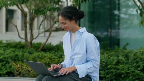Woman Typing on Laptop in Urban Setting