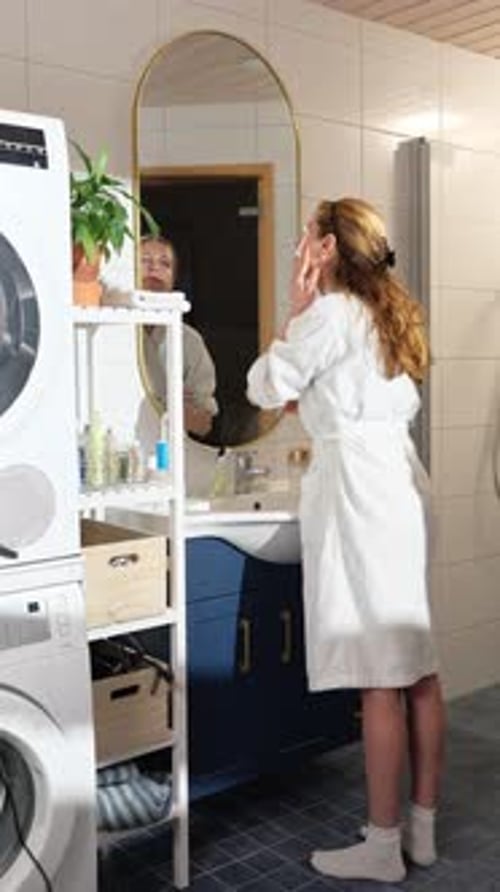 Woman Applies Makeup in Bathroom Mirror