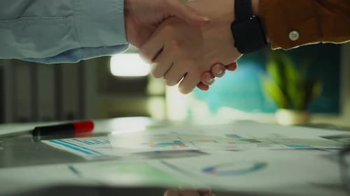 Business Handshake Over Charts and Graphs in Office