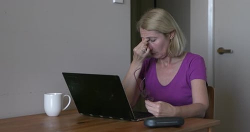 Brillenträgerin reibt müde Augen, überarbeitet am Laptop