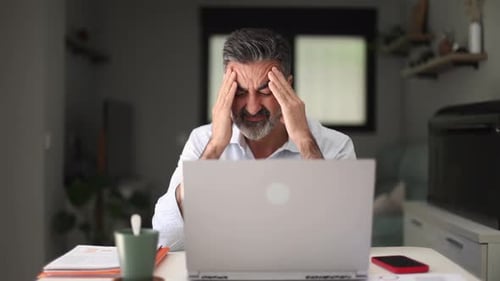 Stressed Man Massaging Temples at Desk in Home
