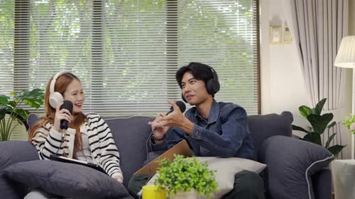 Asian male and female is sitting having fun in the podcast studio at home talking and recording.