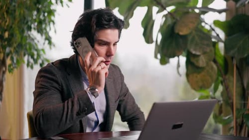 a serious man a businessman works at a laptop in the office communicates with colleagues smartphone