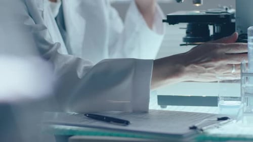 Scientist Using Microscope and Taking Notes in Lab