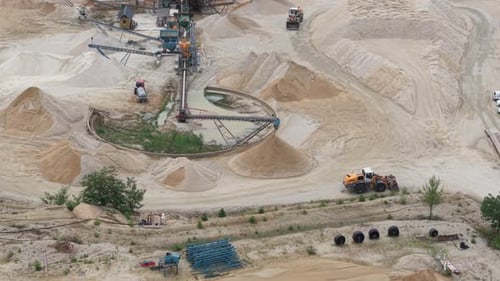 A large sand quarry with heavy including a conveyor system and an orange front loader operating amon