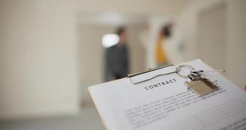 Closeup on a House Sale Purchase Agreement with Keys In the Background a Happily Married Couple