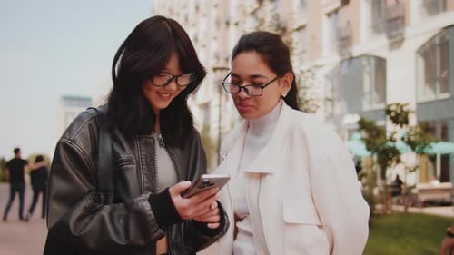 Two Smiling Women Using Phone on City Street