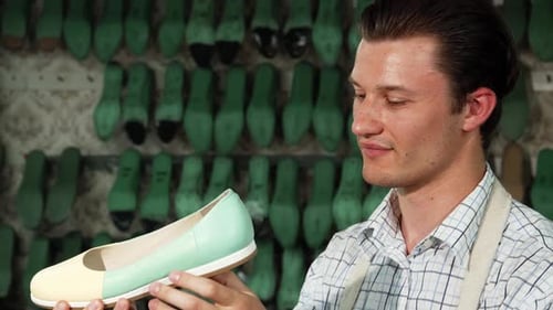 Cheerful Male Shoemaker Proudly Showcasing a Handmade Shoe in His Workshop