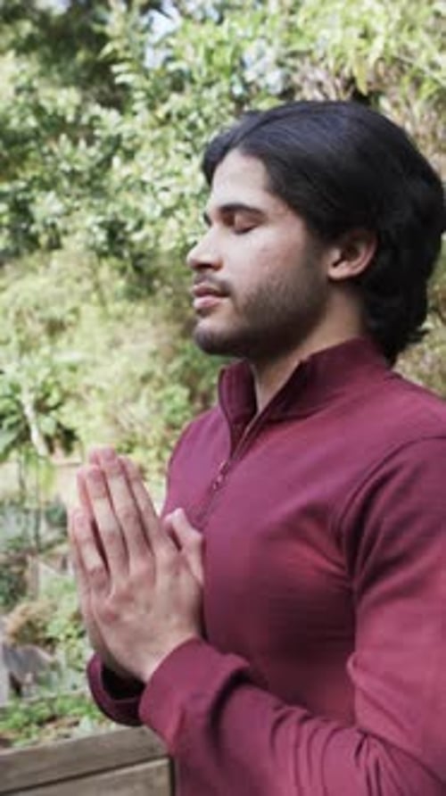 Vertical video of biracial man practicing yoga meditation on terrace in nature, slow motion