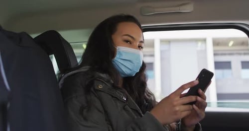 Asian woman wearing face mask using smartphone while sitting in the car