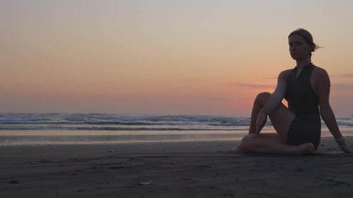 Charmantes Mädchen in Harmonie mit sich selbst sitzt in einer Yoga-Pose auf einer Matte an der Küste