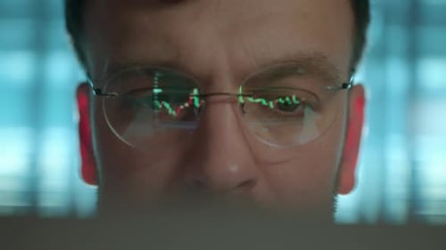 Trader Wearing Glasses arbeitet an einem Laptop-Bildschirm mit Börsencharts und Bitcoin BTC