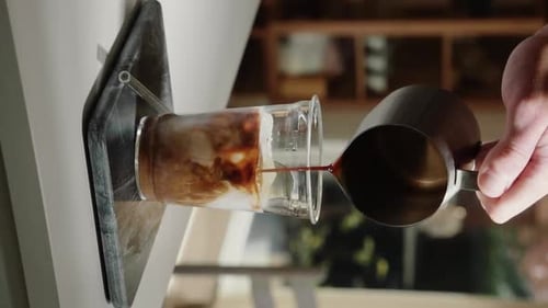 Vertical Video home barista making iced latte pouring espresso shot into glass drinking cup containi