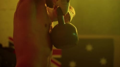 Shirtless Man Lifting Kettlebell in Yellow Light