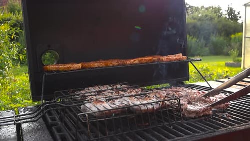 Meat and chicken being grilled on a smoking hot barbecue grill outdoors during summer or autumn day.
