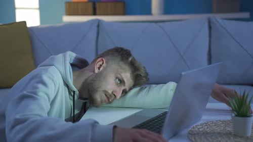 Bored depressed young man using laptop at home. Reluctant mood.