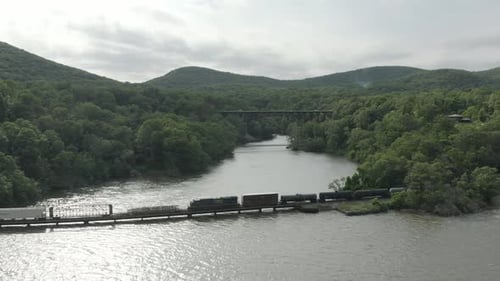 Drohnenaufnahme eines langen Güterzuges, der nach links fliegt und dem Zug folgt, mit einer Brücke im b