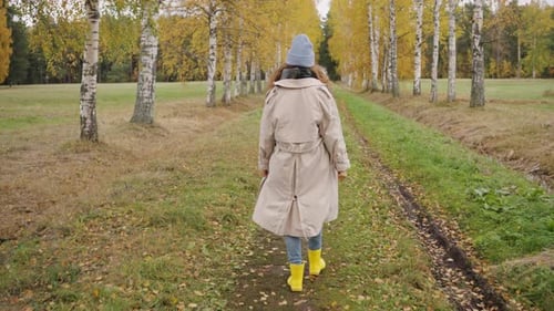 Woman in Trench Coat and Yellow Boots Walking Through Autumn Birch Tree Path